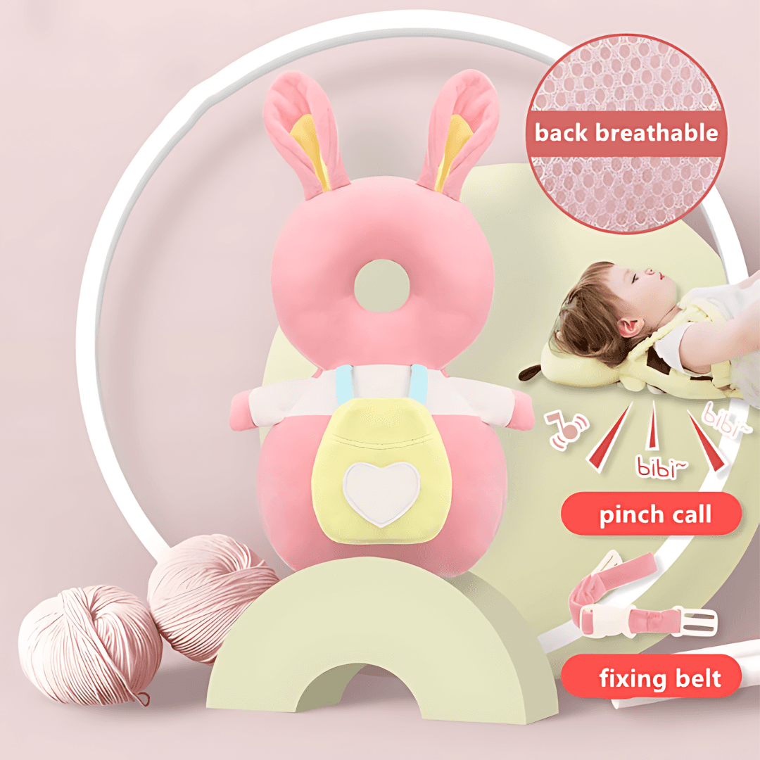 A Protection Backpack, designed as a plush pink and yellow bunny-shaped head protector for babies, doubles as an adorable pillow toy resting on a pastel green crescent. Nearby, a baby sleeps on a soft mattress. The image highlights features such as the breathable back, pinch call, and fixing belt. Balls of yarn are seen in the background.