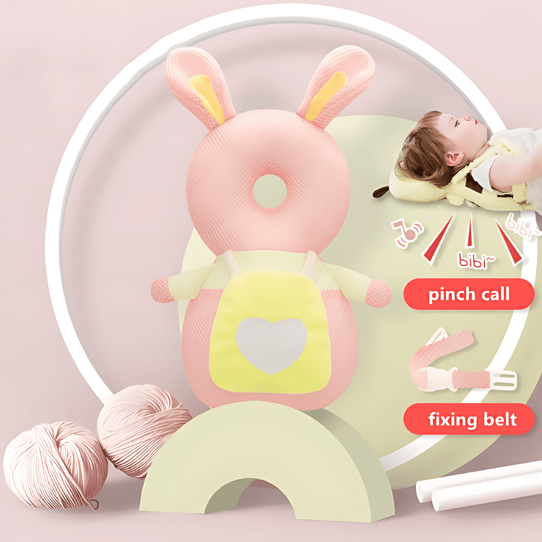 A product called the "Protection Backpack" features a stuffed toy shaped like a pink rabbit with yellow ears, resting on a stand designed to resemble pastel green and pink rainbows. Nearby, there is a peacefully sleeping baby, various knitting supplies, and text labels marked "pinch call" and "fixing belt." The light pink background enhances its adorable design for babies.